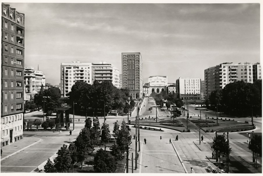 Piazza Fiume con la stazione centrale in lontananza, al centro dell'immagine. La Stazione Centrale di Milano è rialzata per superare il livello stradale cittadino, eliminando i passaggi a livello che bloccavano il traffico urbano. L'elevazione dei binari consentì di raccordare agevolmente la nuova stazione di testa alla cintura ferroviaria periferica, garantendo uno scorrimento fluido e sicuro dei treni. Fonte: Archivio Insubrica Historica